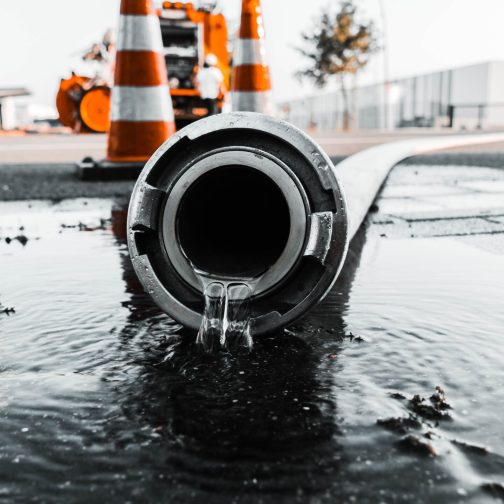 A selective closeup shot of a gray pipe with water coming out its hole